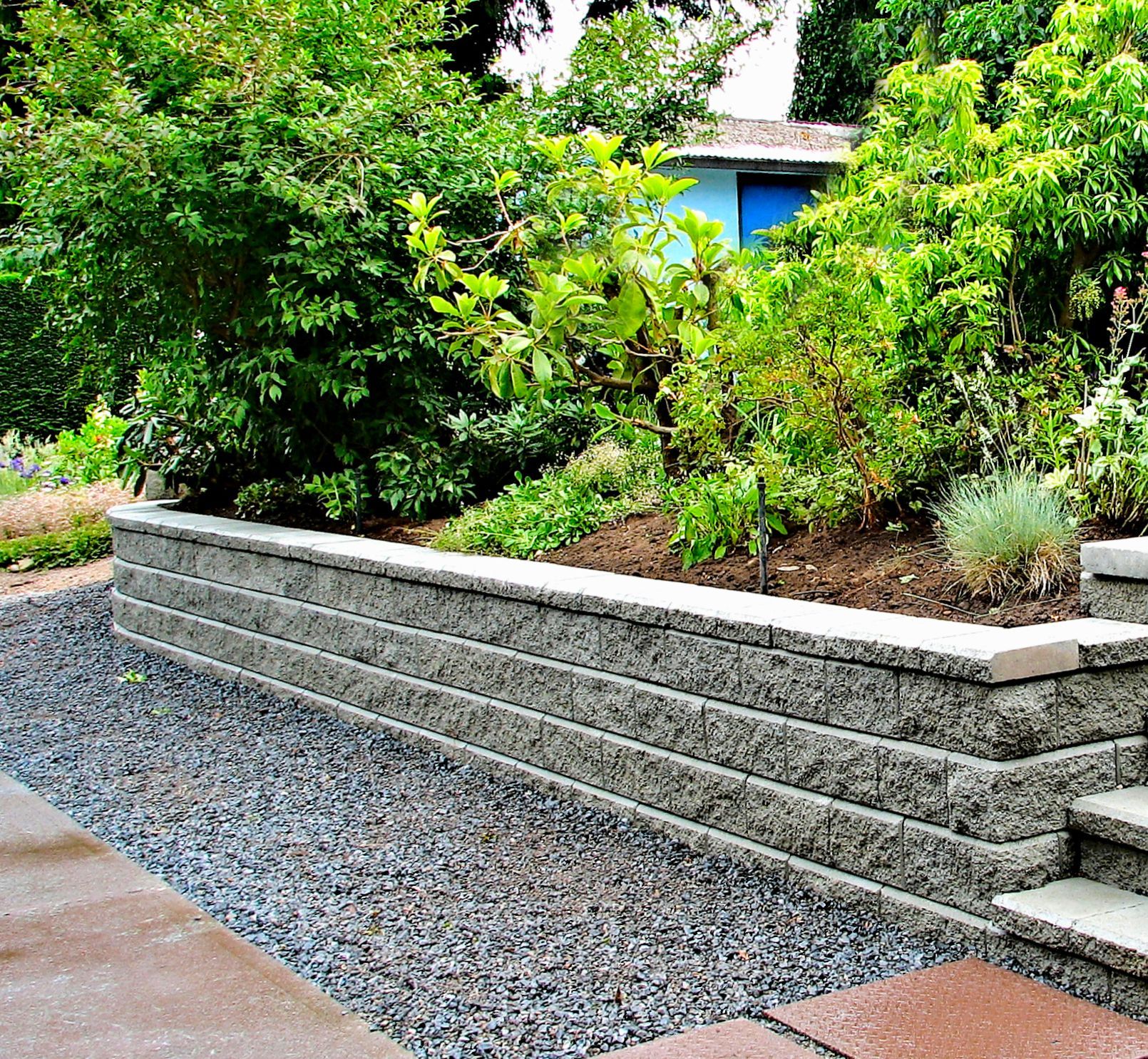 A stone wall is surrounded by gravel and trees