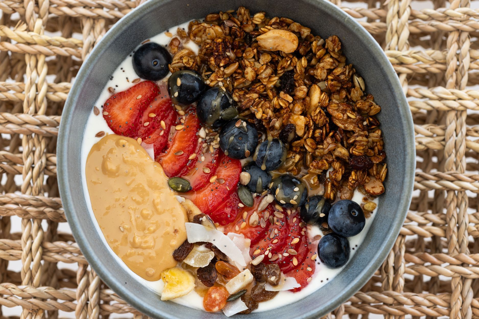 Un tazón de granola cubierto con fresas, arándanos y mantequilla de maní sobre un mantel individual tejido.