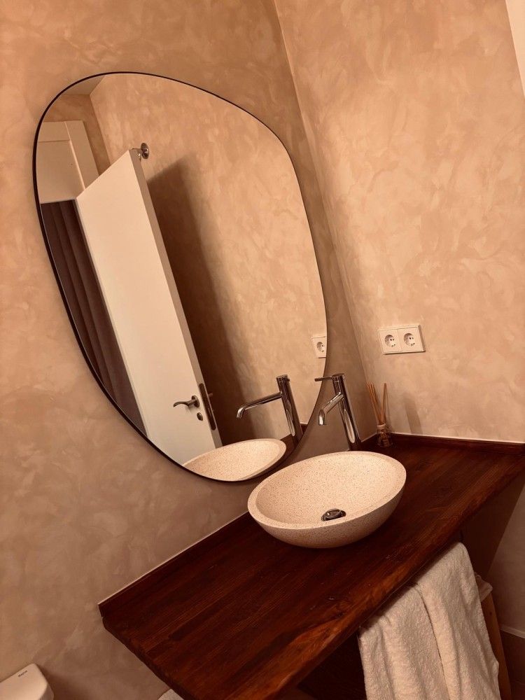 Espejo redondo sobre un tocador de madera con lavabo y grifo blancos en un baño de color beige.