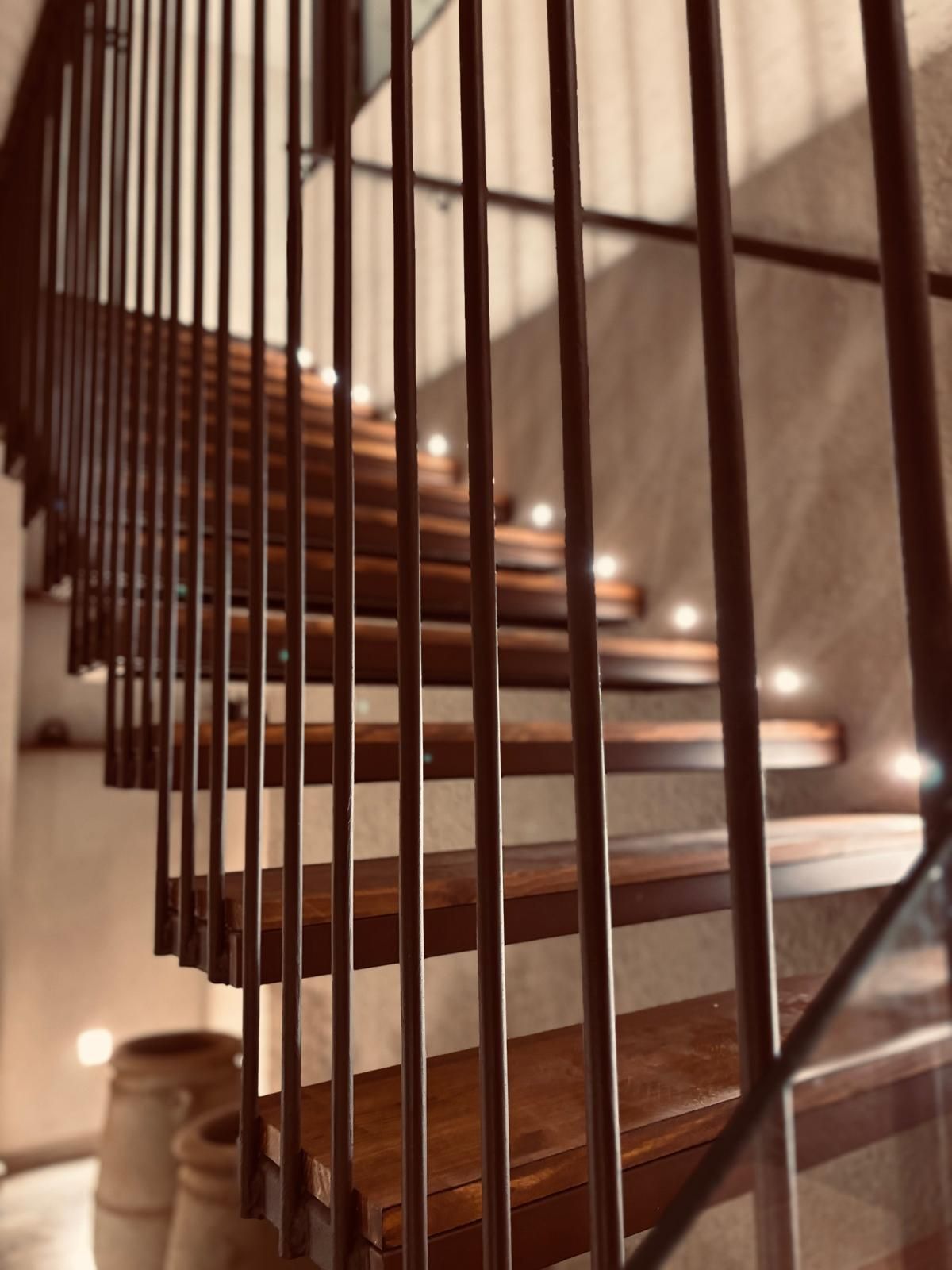 Escalera curva de madera con barandillas verticales y apliques de pared cálidos en un interior con iluminación tenue.