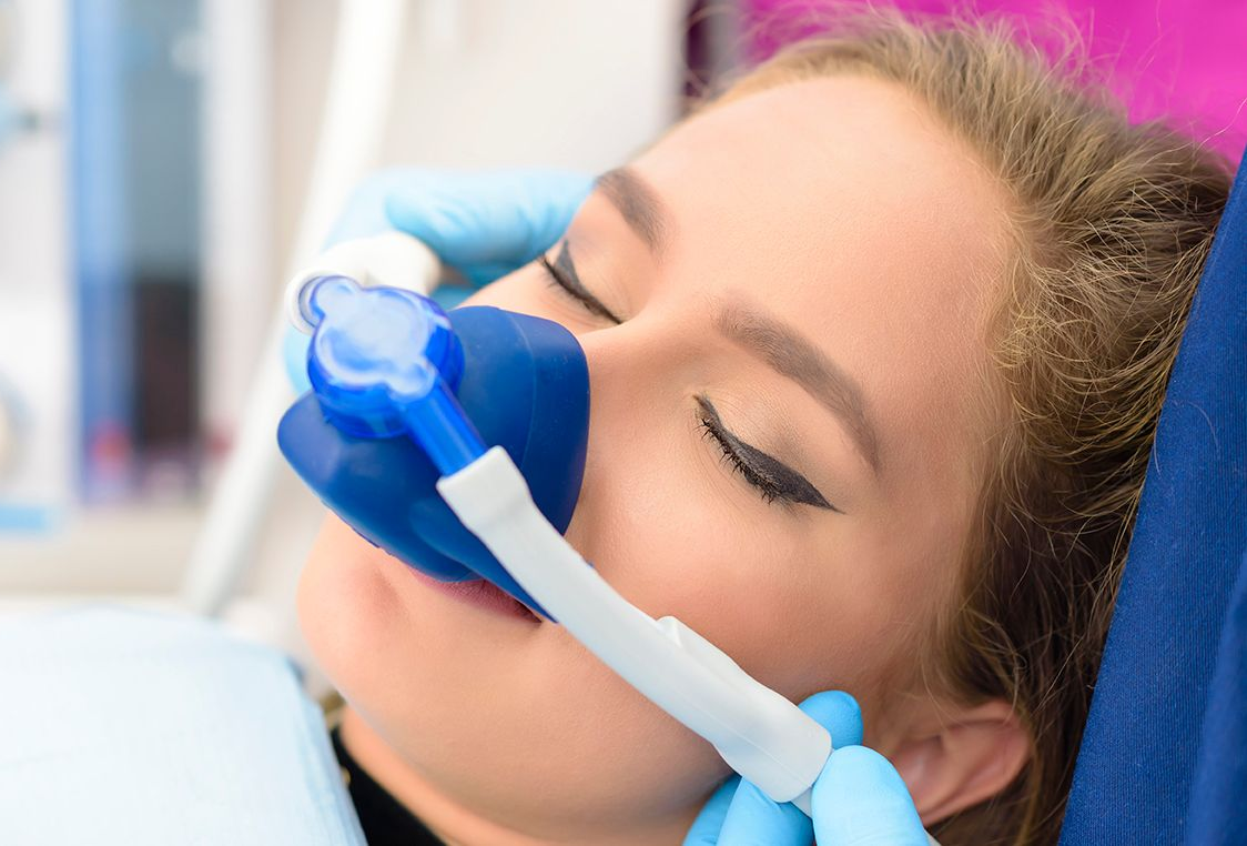 Vrouw in tandartsstoel met blauw zuurstofmasker over neus, ogen gesloten.