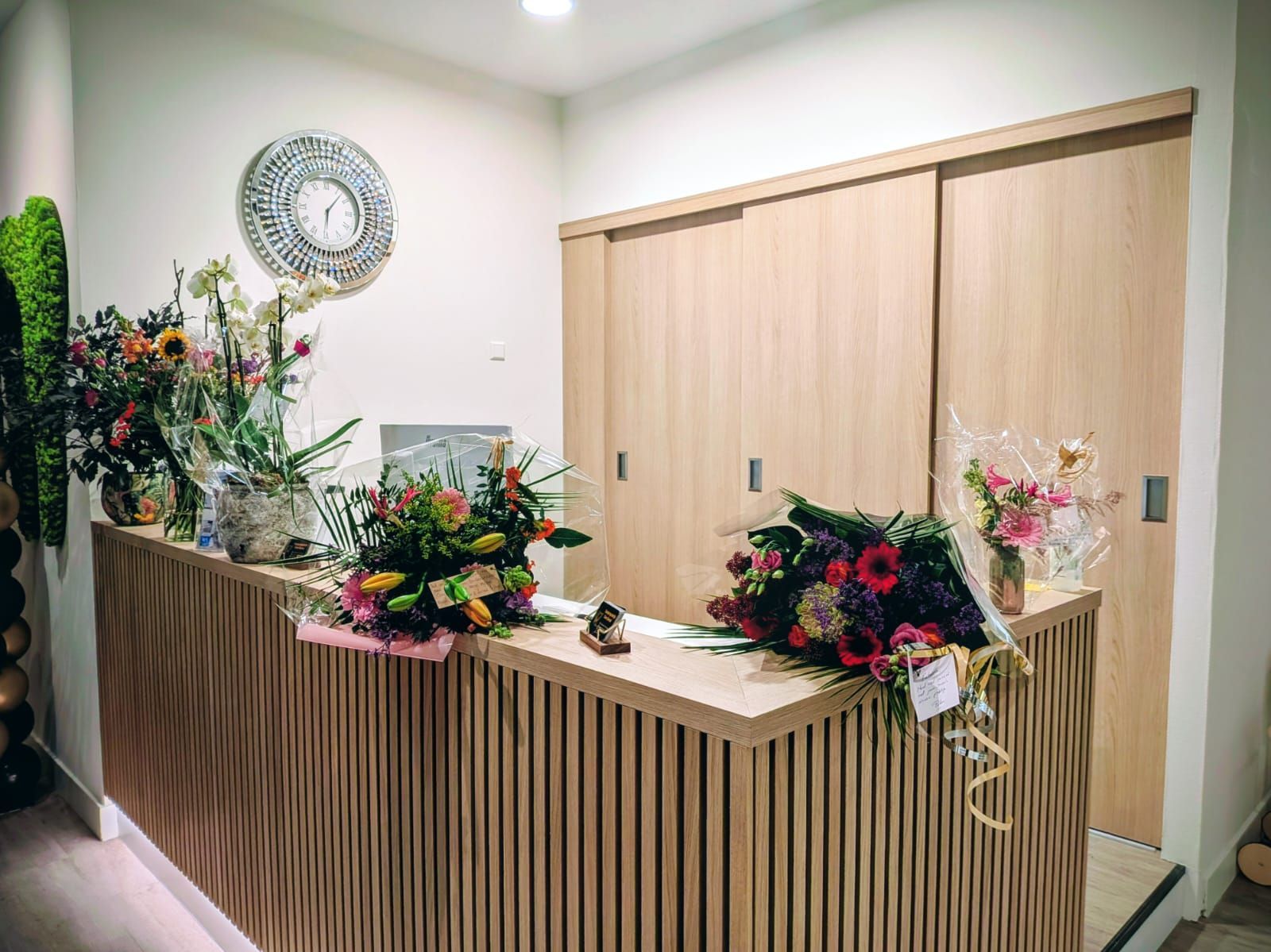 Receptiebalie met bloemen, lichte houten lambrisering en schuifdeuren.