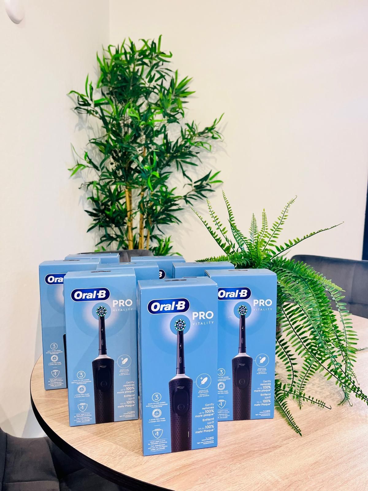 Dozen van Oral-B Pro elektrische tandenborstels op een tafel, met planten op de achtergrond.