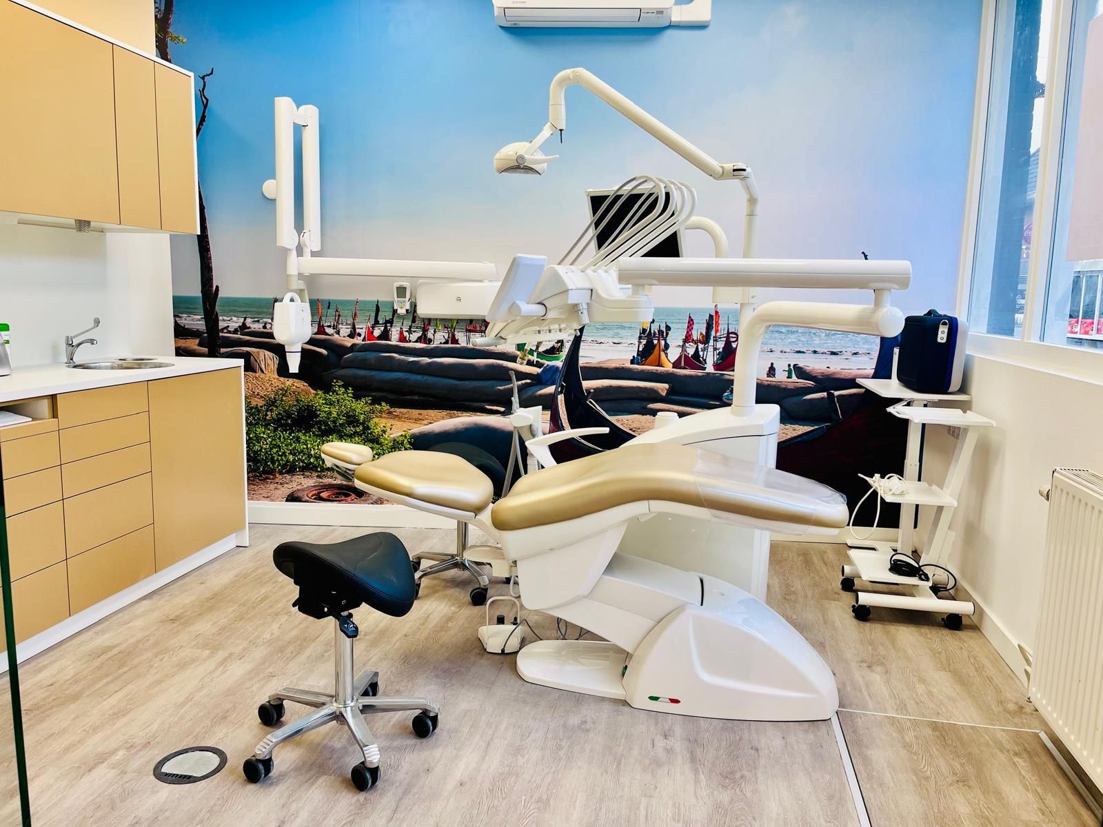 Tandartspraktijk met tandartsstoel, apparatuur en een muurschildering met strandthema.
