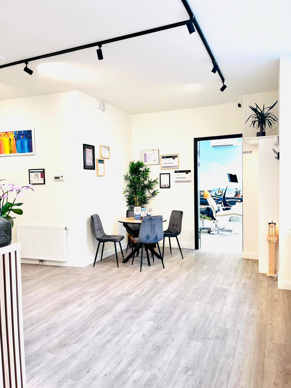 Ontvangstgedeelte met tafel, stoelen, planten en een deur die toegang geeft tot een tandartspraktijk.