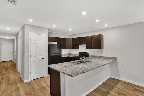 Kitchen with brown cabinets, black appliances, granite countertop, and wood flooring.