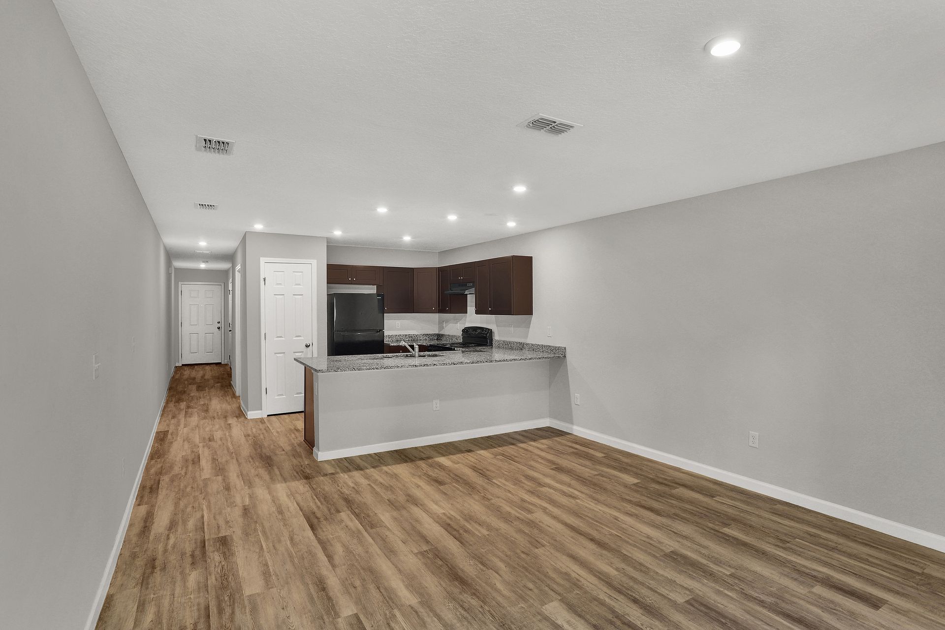 Empty apartment interior with kitchen, cabinets, and wood flooring.
