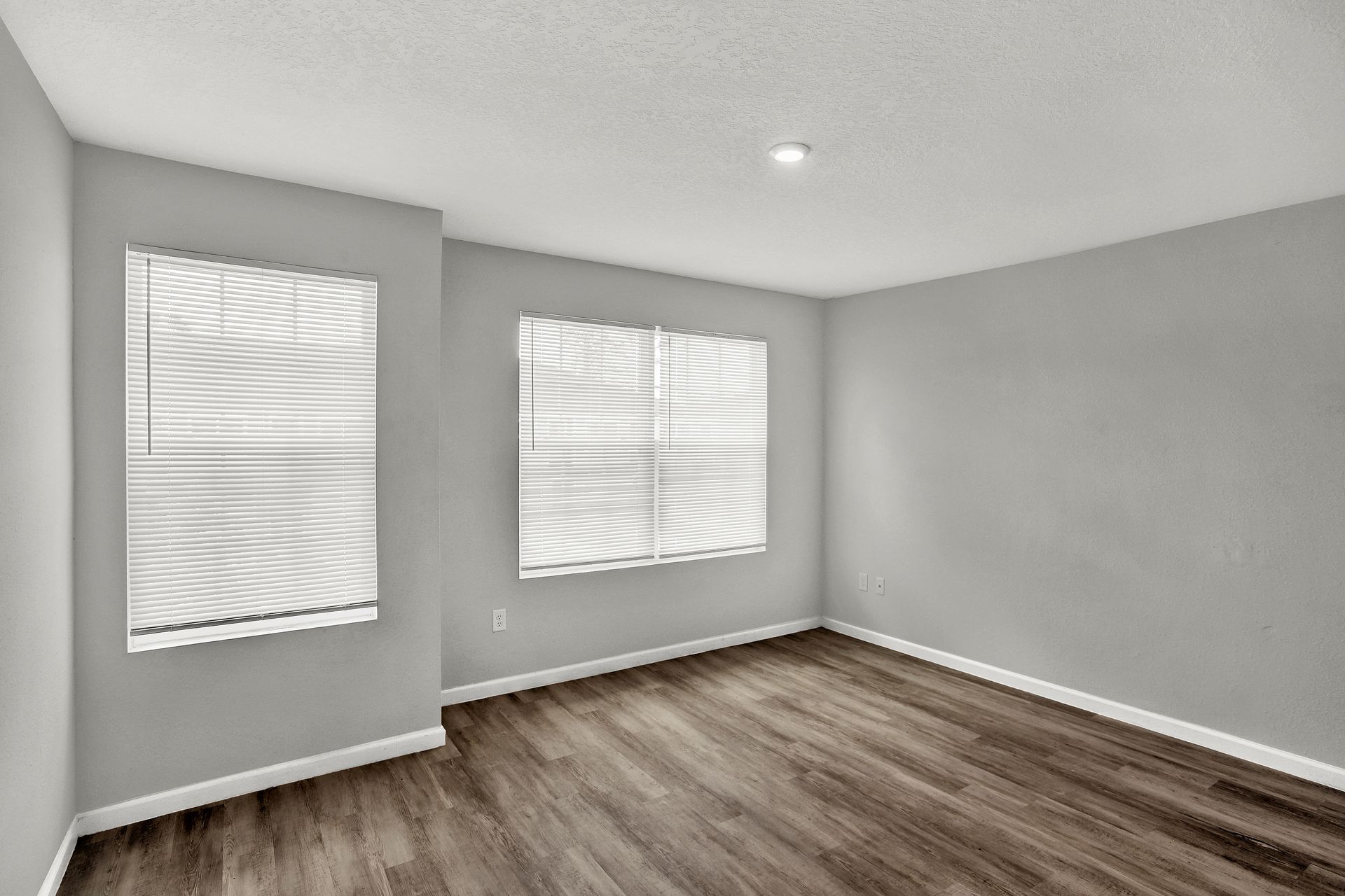 Empty room with gray walls, two windows with blinds, wood-look floor, and white trim.