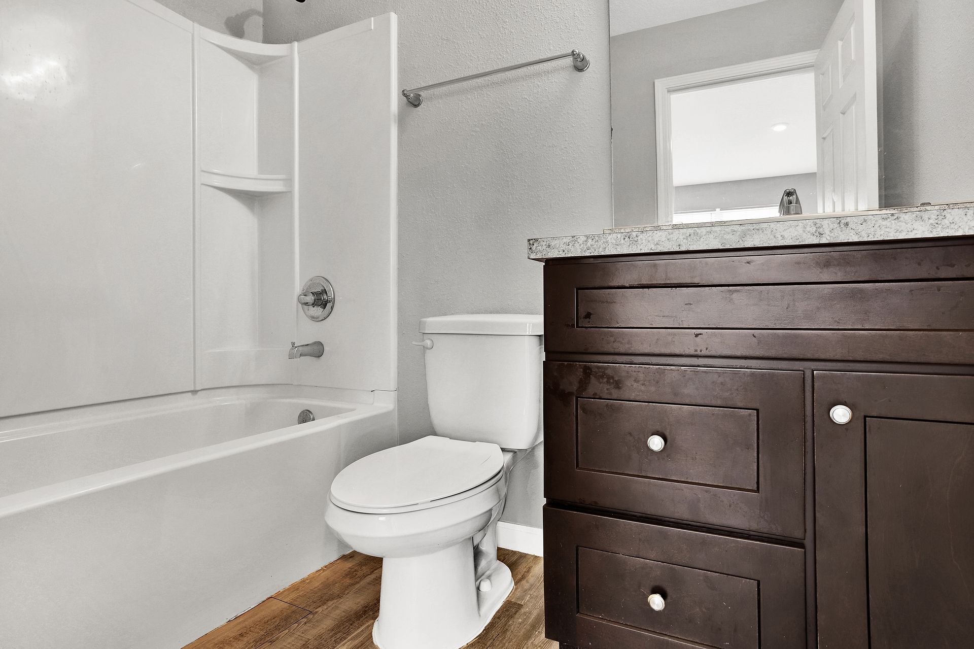 Bathroom with a white tub and toilet, dark brown vanity, and a gray textured wall.