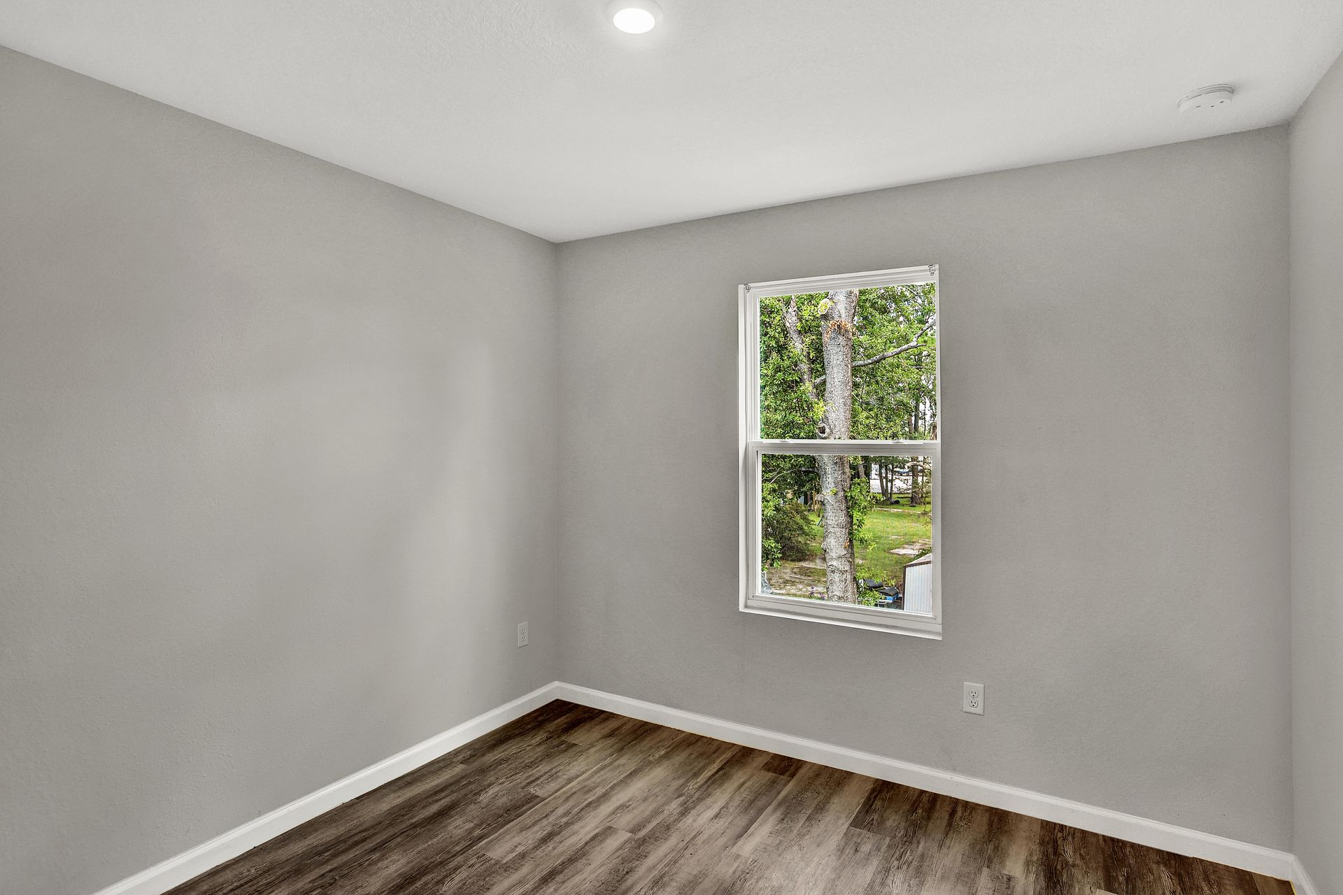 Empty room with gray walls, wood floor, and window.