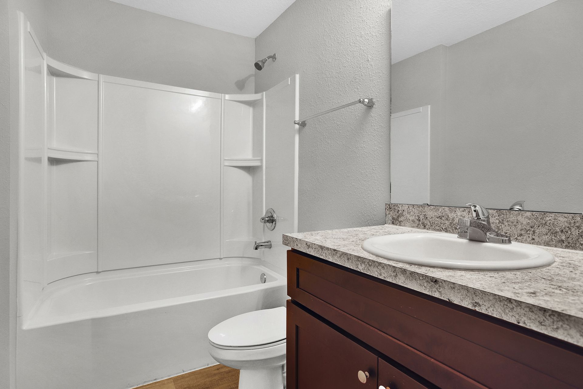 Bathroom with white tub/shower combo, dark vanity, and textured wall.