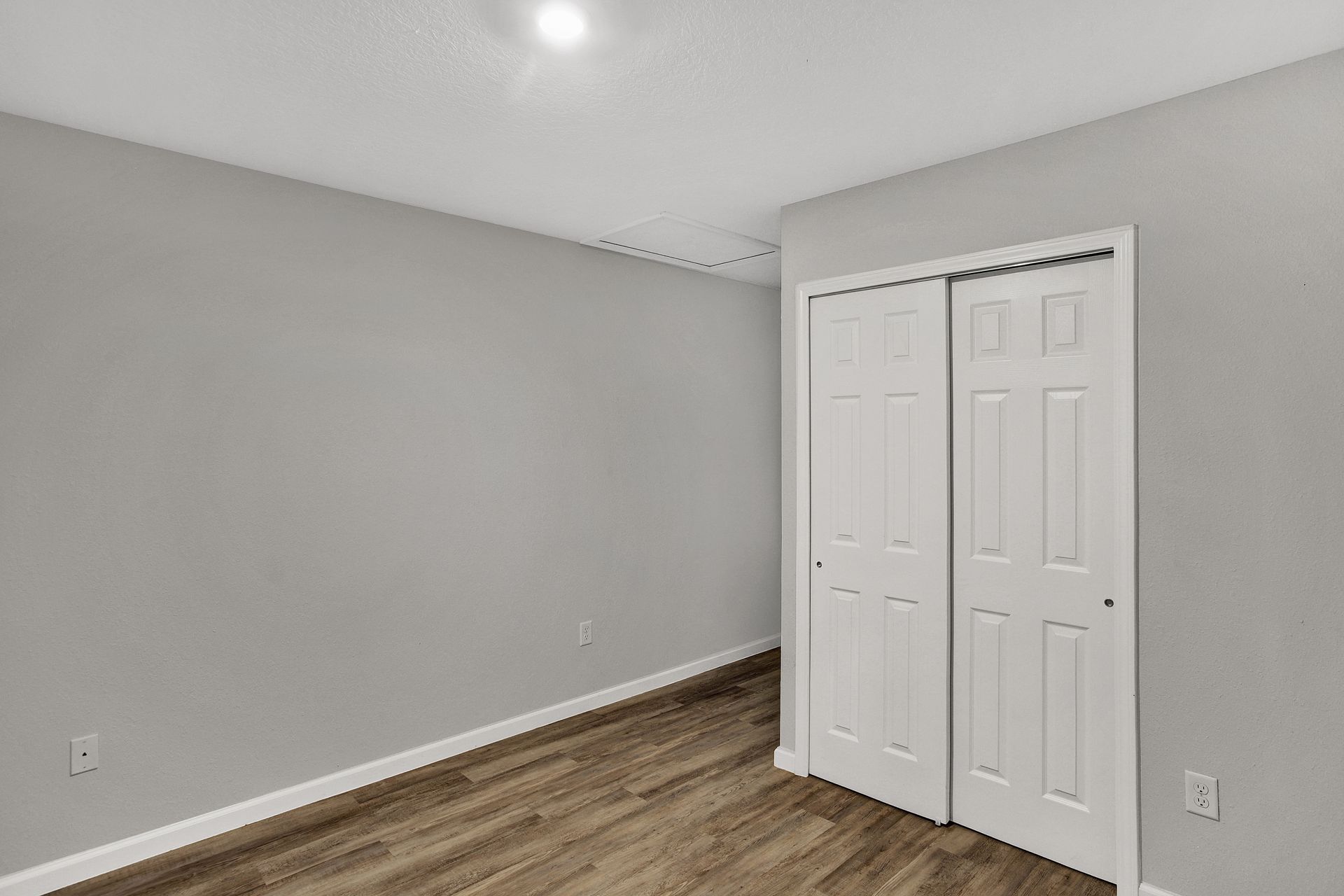 Empty bedroom with gray walls, white closet doors, and wood-look flooring.