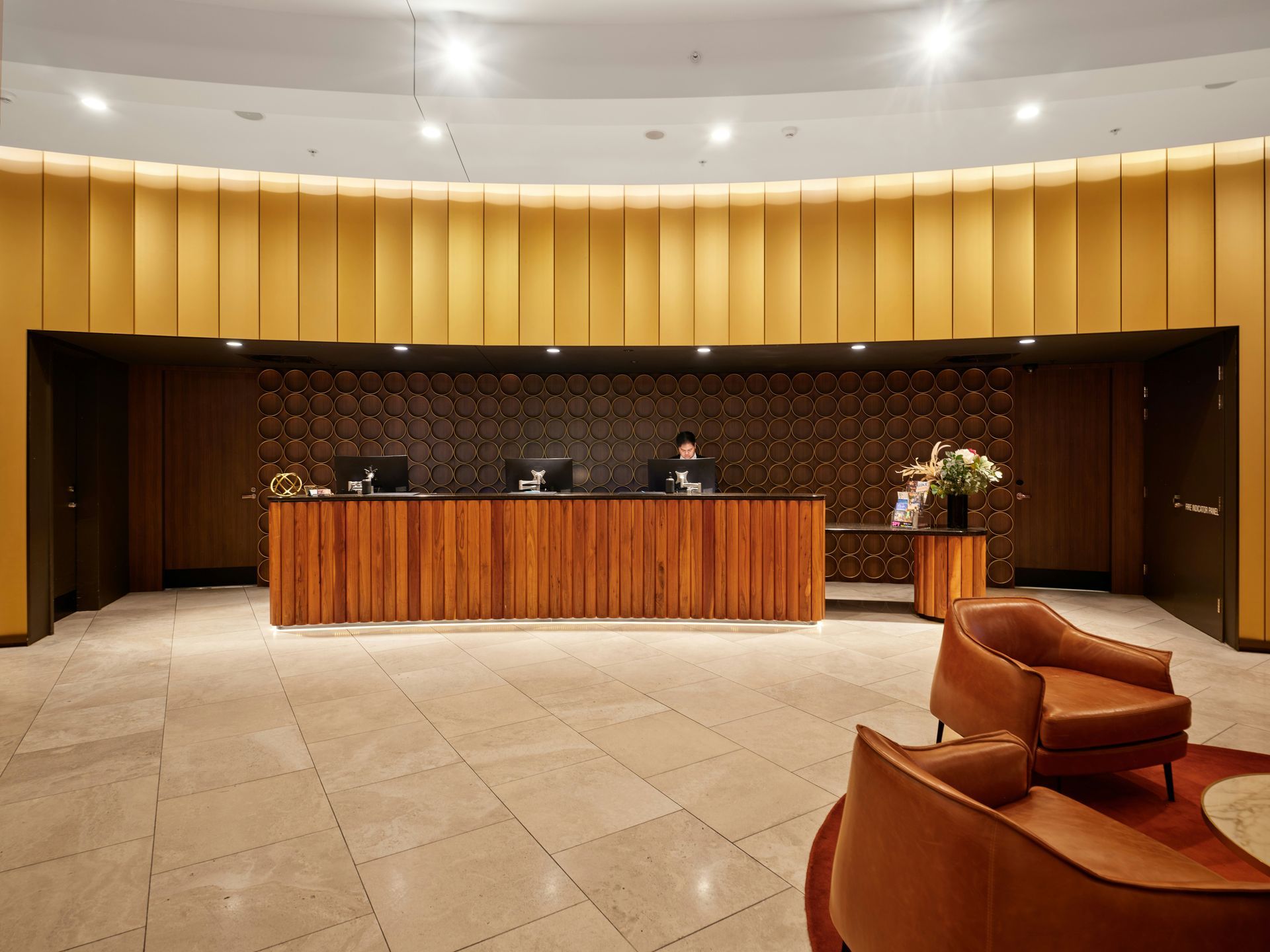 Hotel reception desk with wood paneling, mustard walls, and brown leather chairs.