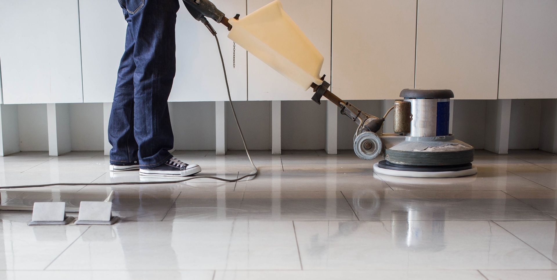 A person is cleaning a tiled floor with a machine.