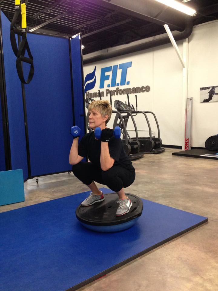 A woman squatting with dumbbells in a gym with a sign that says fit