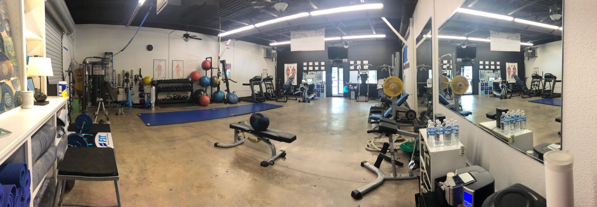 A large gym filled with lots of exercise equipment and mirrors.