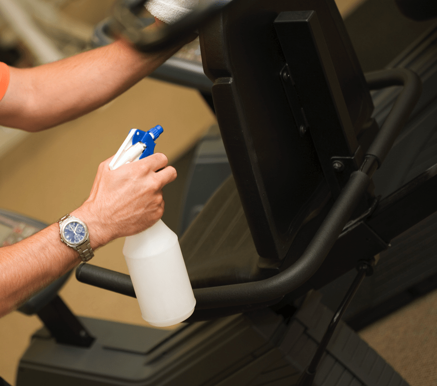 A man wearing a watch is cleaning a treadmill with a spray bottle