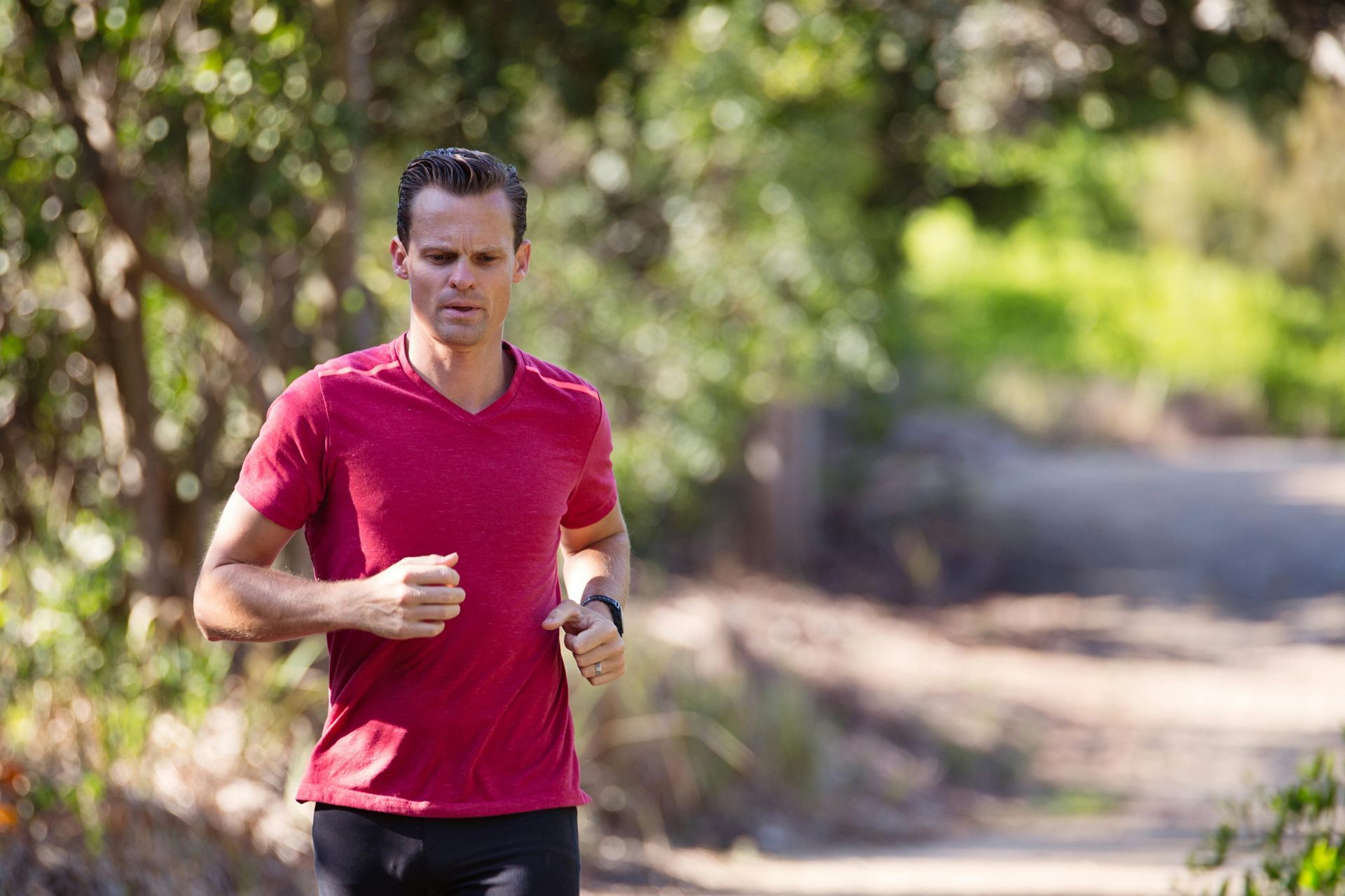 A man in a red shirt is running on a path in the woods.