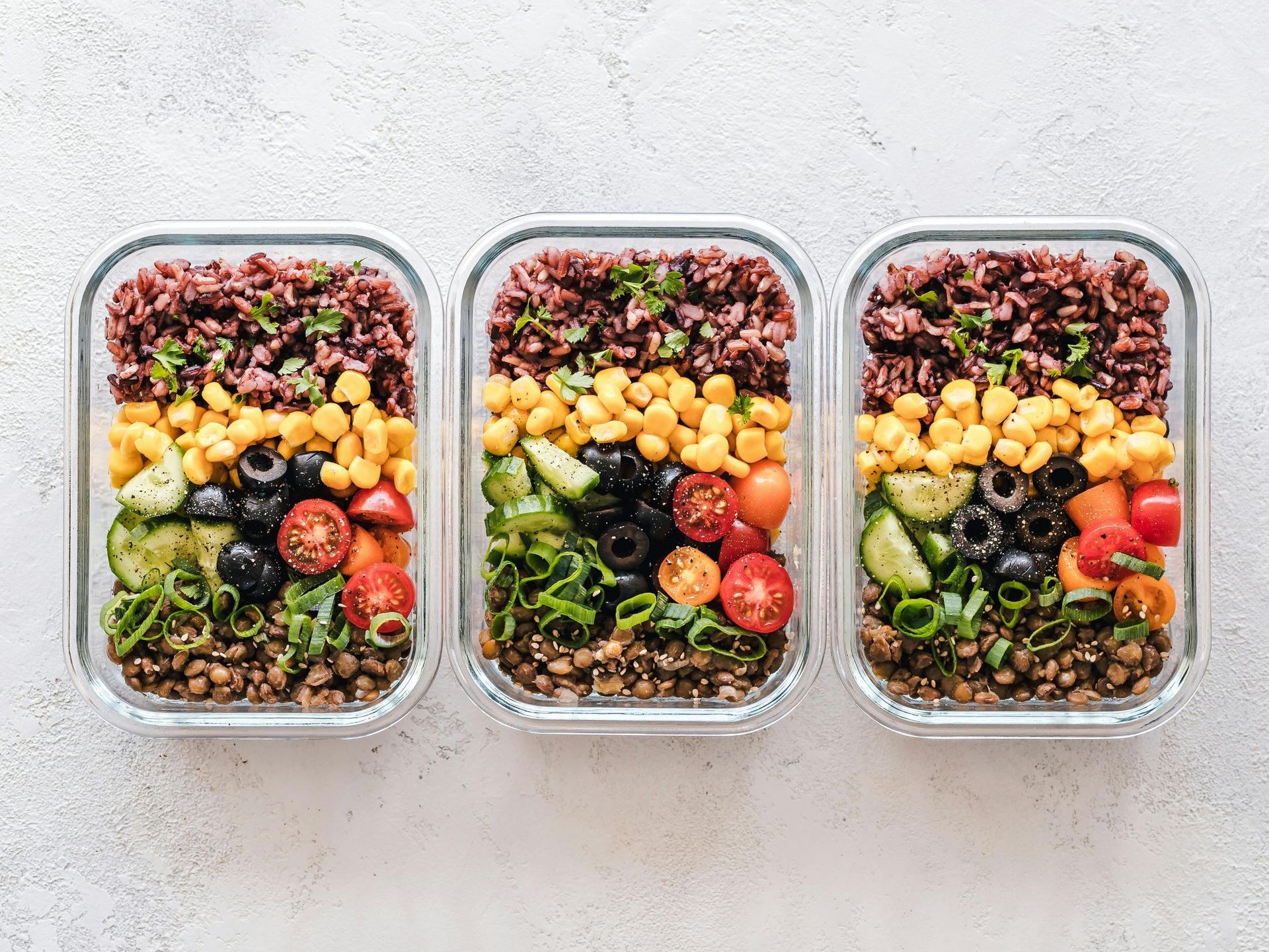 Three glass containers filled with different types of food on a table.