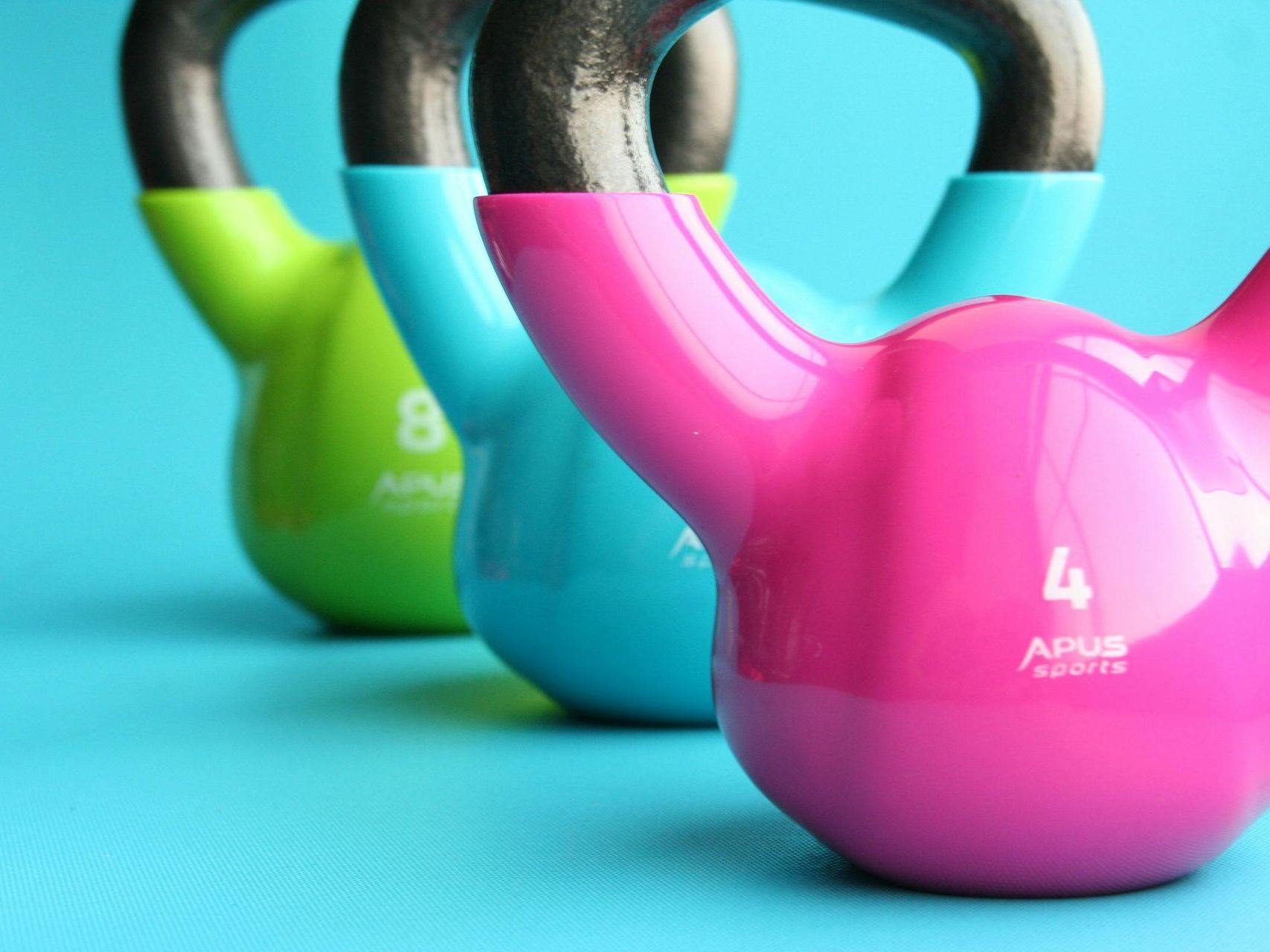 A pink kettlebell is next to a green kettlebell and a blue kettlebell