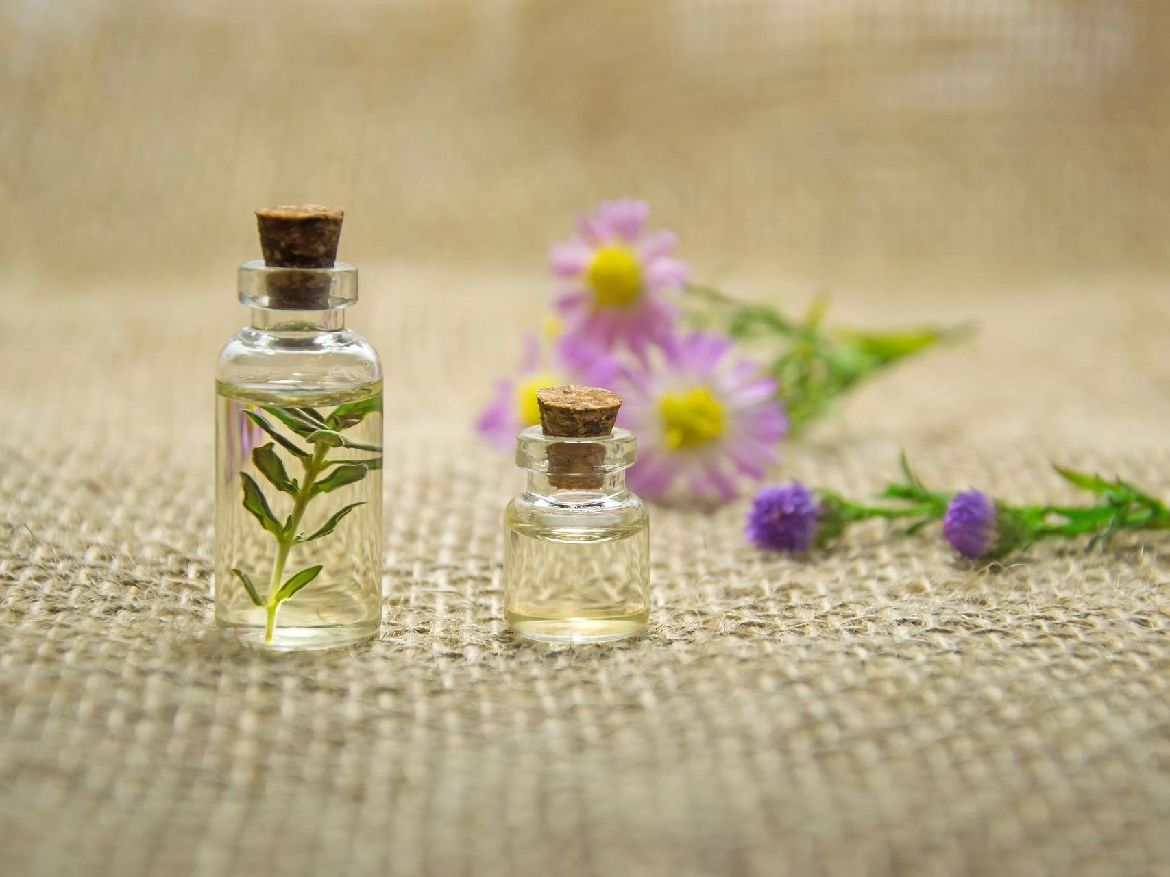 Two small bottles of essential oil with flowers in the background.