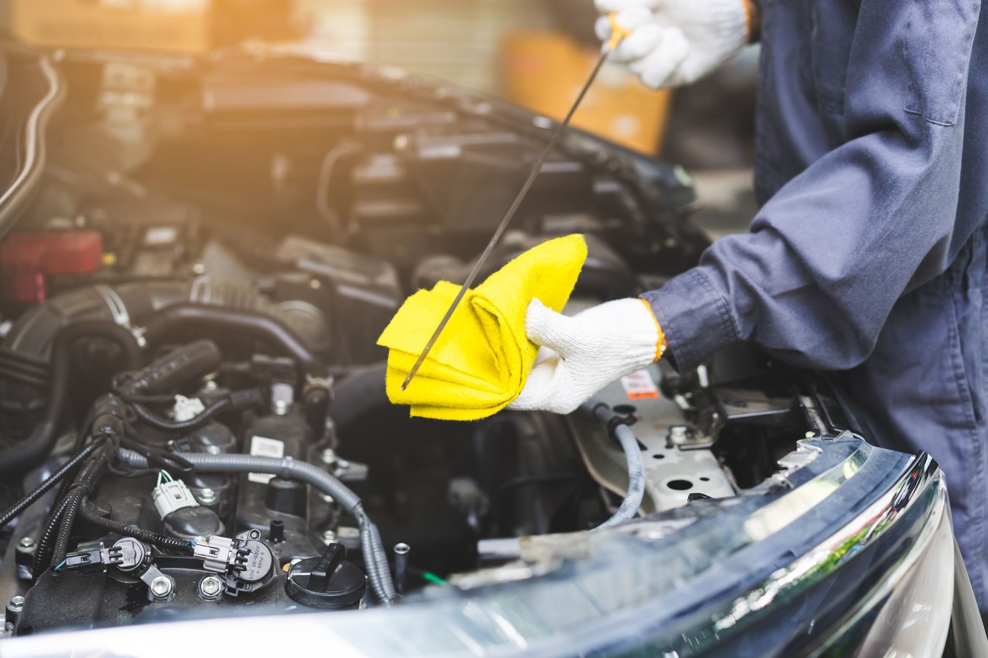 Mechanic checking car engine oil with a dipstick and yellow cloth. | Auto Check Elite