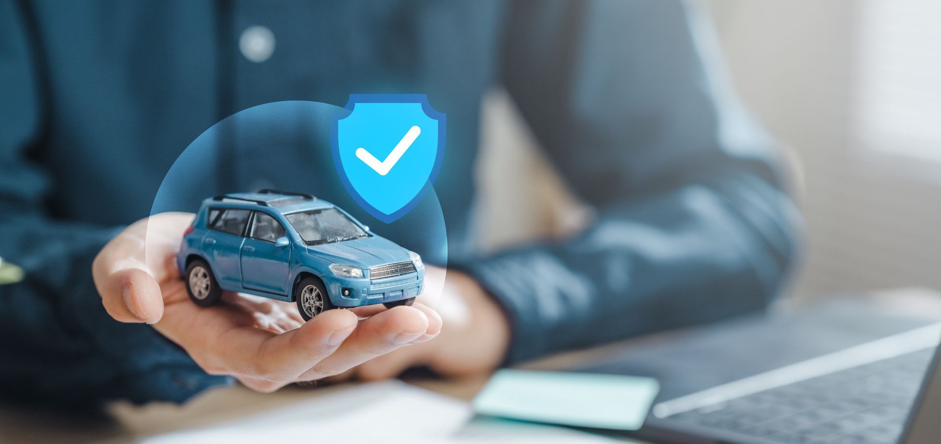 A hand holding a toy car with a glowing shield icon above it, suggesting insurance or protection. | Auto Check Elite