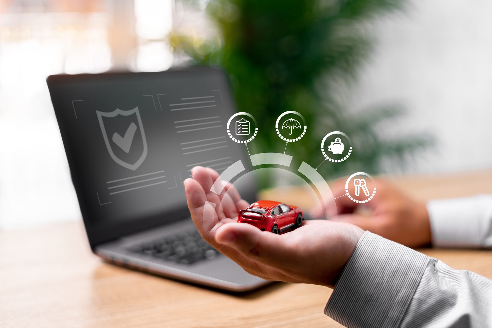 Person holding toy car, surrounded by digital car insurance icons, in front of a laptop. | Auto Check Elite