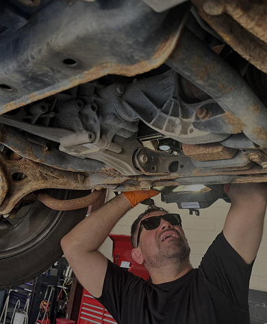 Mechanic working under a car, illuminated by a light. | Auto Check Elite