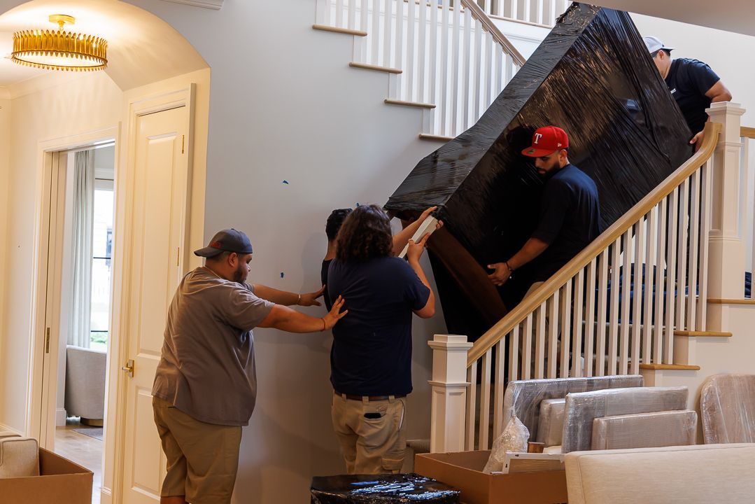 Movers carrying large furniture up a staircase inside a house.