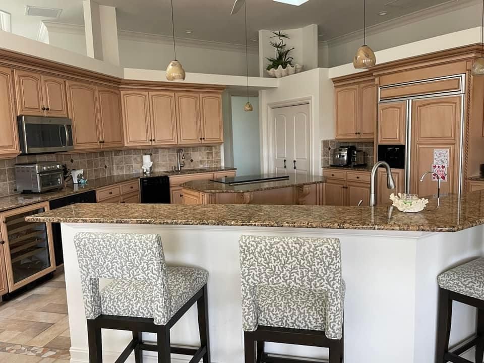 A kitchen with wooden cabinets , granite counter tops , and stools.
