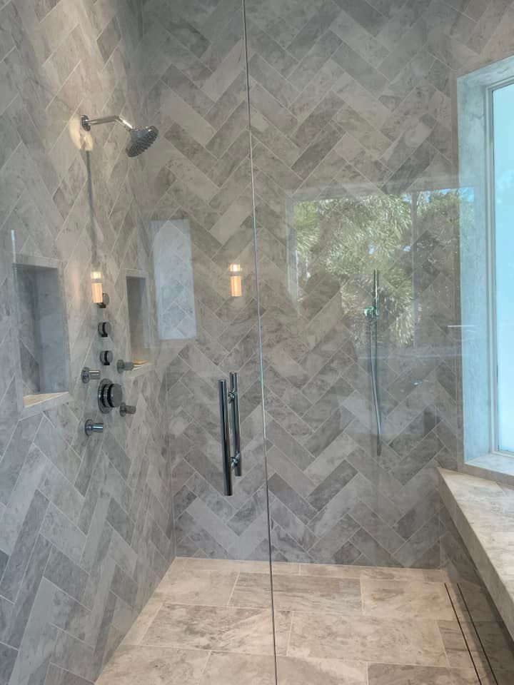 A bathroom with a walk in shower with a glass door and a window.