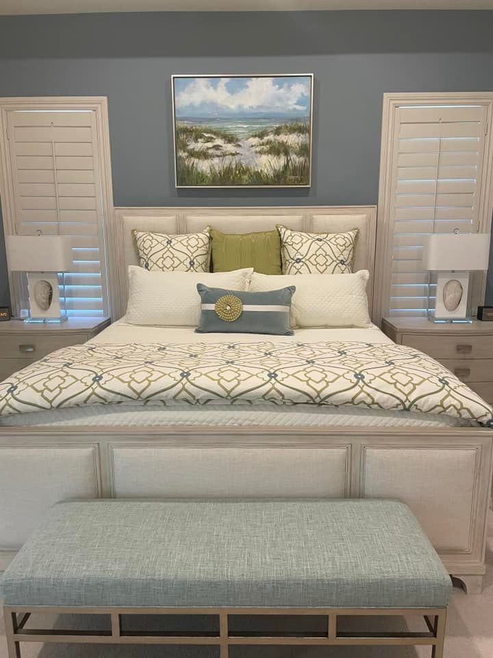 A bedroom with a bed , two nightstands , a bench and a painting on the wall.