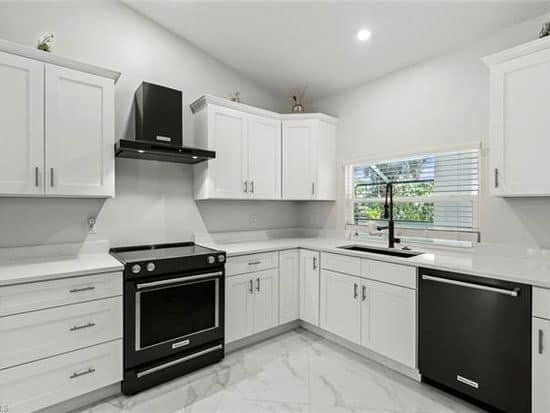 A kitchen with white cabinets , black appliances , and a window.