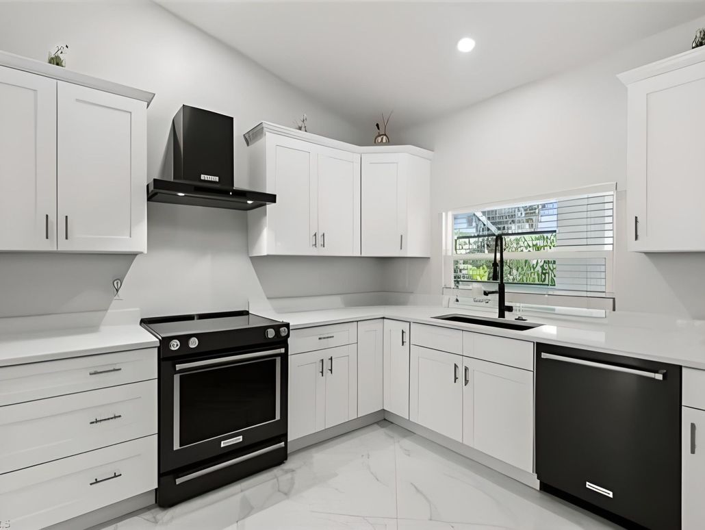 A kitchen with white cabinets , black appliances and a window.