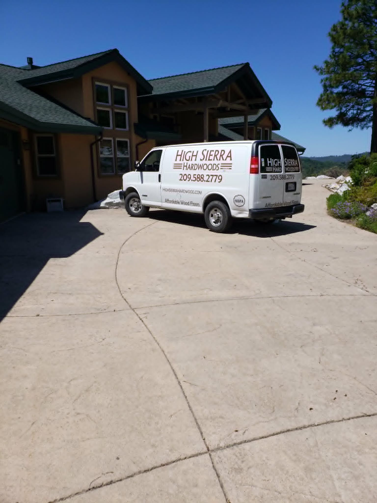 White service van parked on a driveway beside a large house on a sunny day