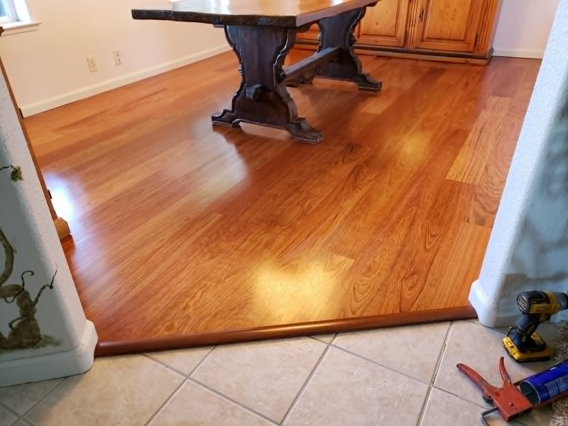 Wooden dining room floor with a dark table, viewed from a tiled entryway