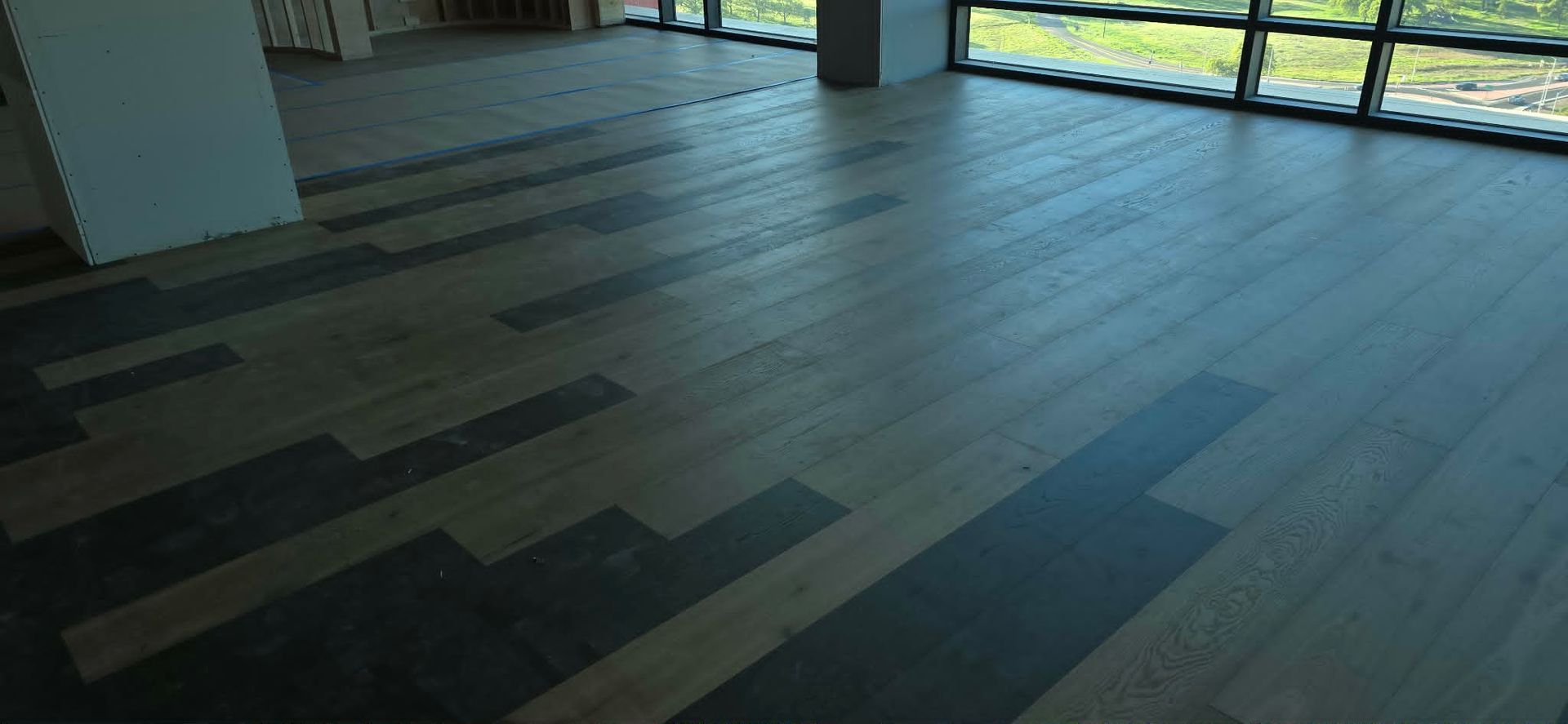 Empty room with dark wood-patterned flooring and large windows letting in daylight.