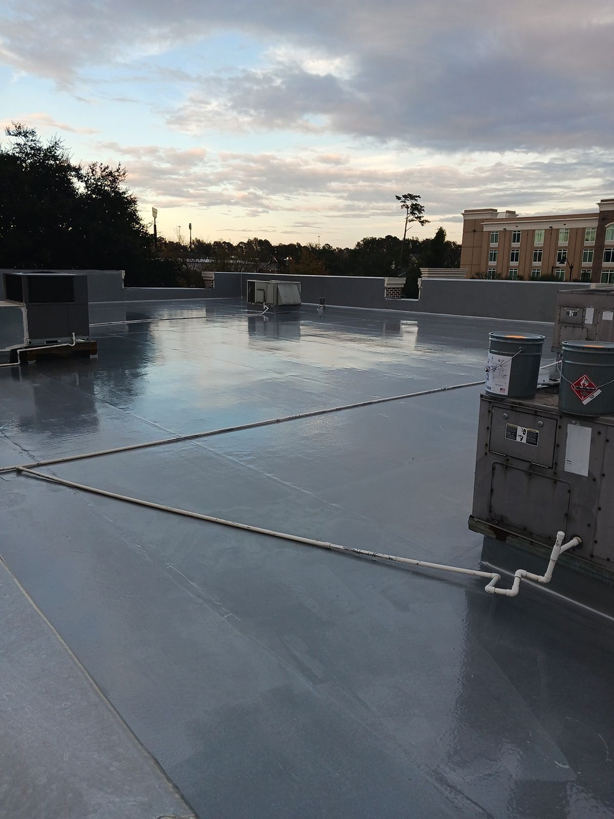 Flat, gray commercial rooftop with HVAC units, pipes, and a cloudy sky.