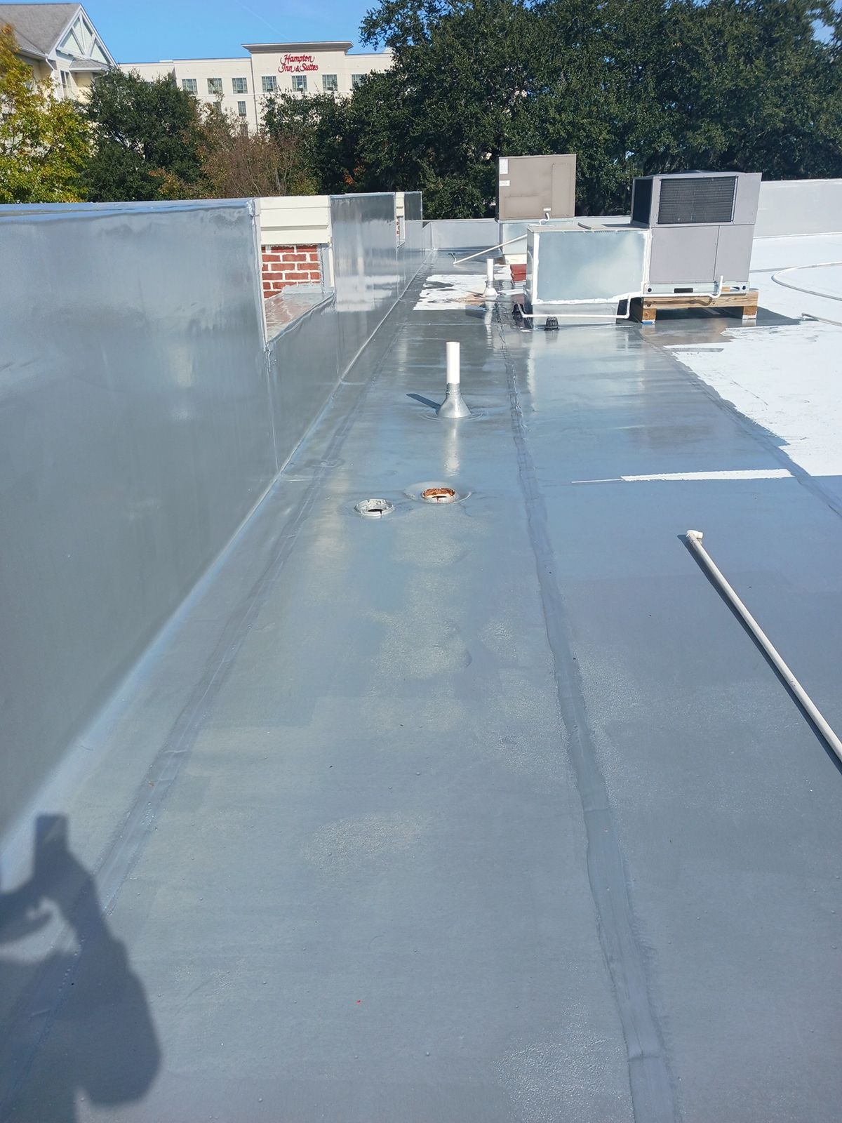 A gray flat commercial roof with metal edging, vents, and a drain pipe on a sunny day.