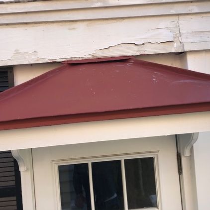 Red awning above a white door and window, attached to a weathered white building.