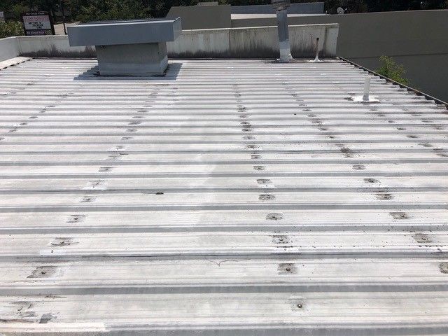 Flat, corrugated metal roof with vents and a pipe.