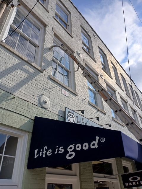 Life is good store with blue awning, building facade, ladder to upper windows, sunny day.
