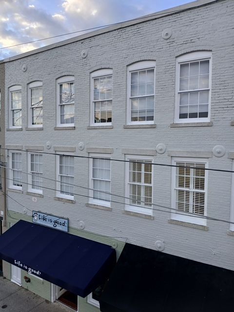 Three-story building with gray painted brick, white-framed windows, and awnings over ground-floor storefronts.