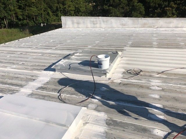 White-painted corrugated metal roof with a bucket, cord, and a person's shadow on a sunny day.