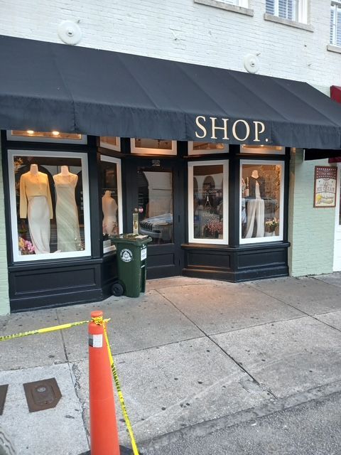 Shop storefront with black awning, glass display windows, and mannequins inside. Yellow caution tape in front.