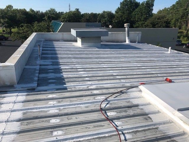 A flat metal roof with a white coating, vents, and equipment on a sunny day.