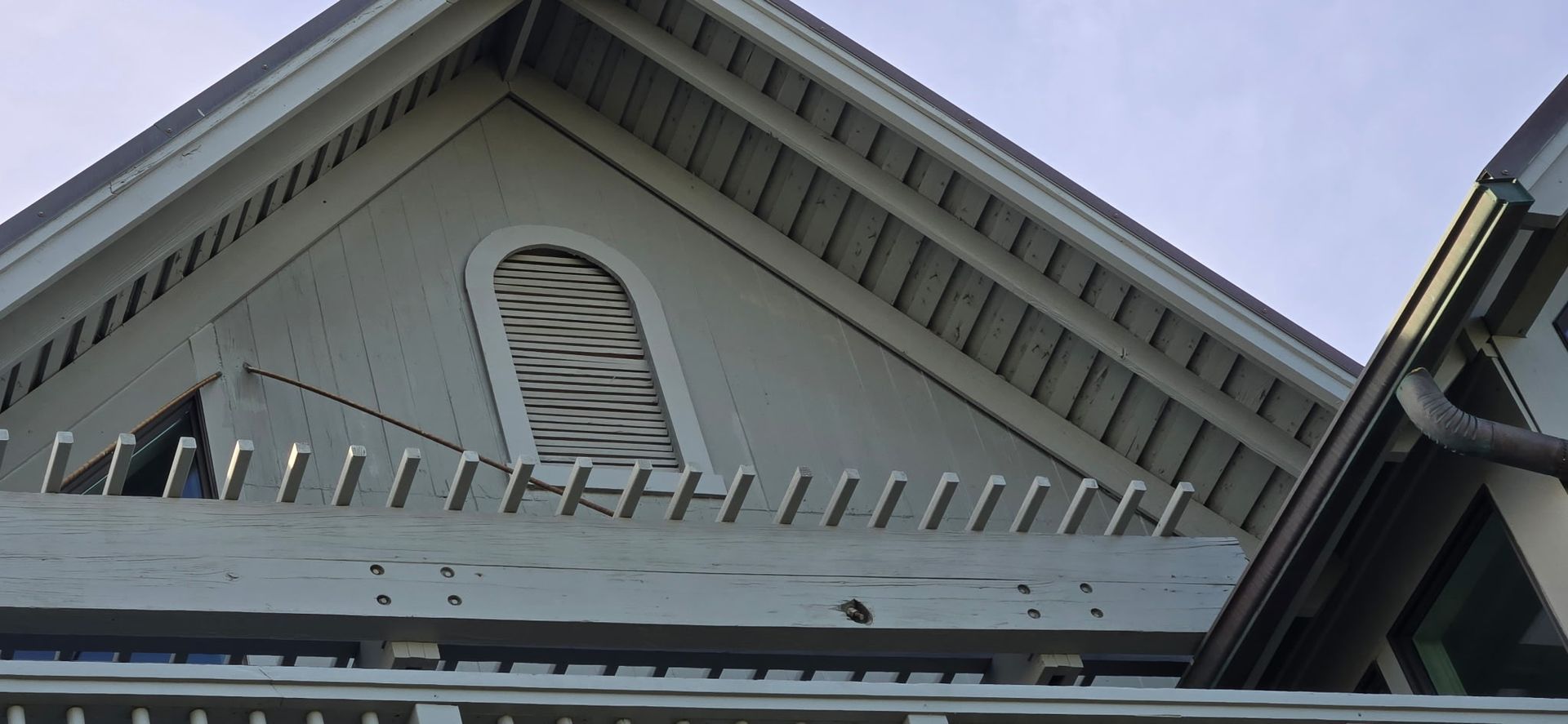 Exterior of a gray house, the roofline with an arched window, and a row of posts.
