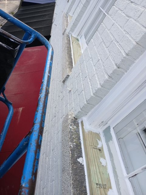 A blue lift next to a white brick wall, wooden trim, and windows, possibly during construction.