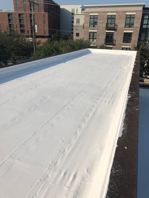 White flat roof, newly coated, bordered by a dark edge. Buildings and trees in the background.